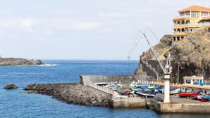 Un port côtier où sont amarrés des bateaux, un phare et un bâtiment doté de balcons donnant sur l’eau.