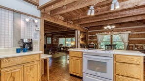L’intérieur d’un chalet rustique, avec des poutres en bois, une cuisine équipée d’un poêle et de placards, et un coin repas comprenant une table et des chaises.