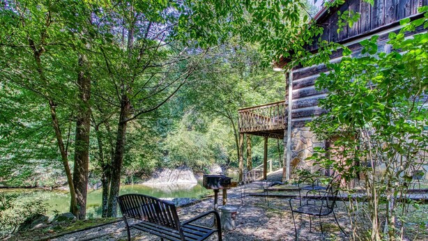 Un chalet rustique doté d’une terrasse en bois donnant sur un étang, le tout entouré d’une forêt dense.
