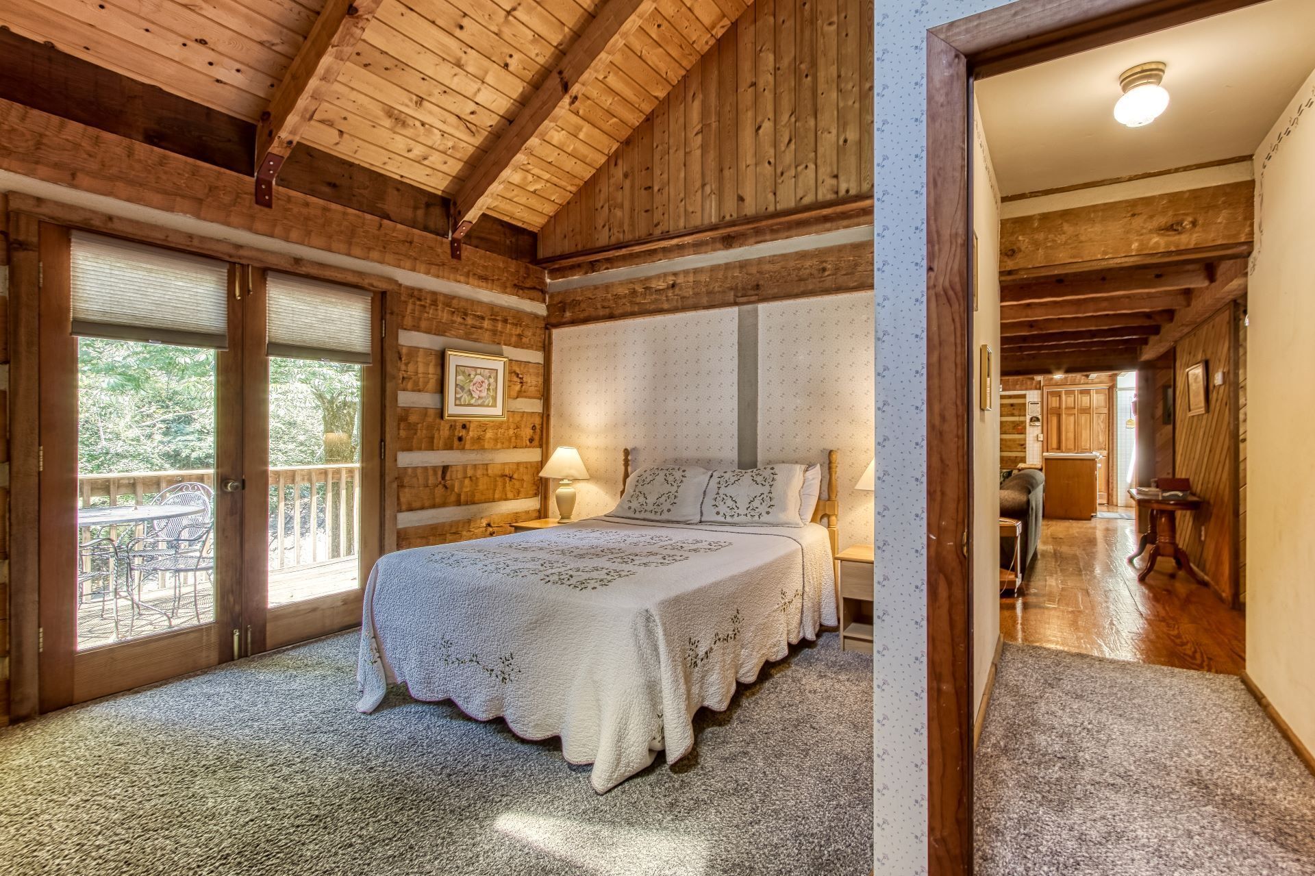 Ein Schlafzimmer mit einem großen Bett, einem Nachttisch, einem Fenster mit Jalousien und Blick ins Freie.