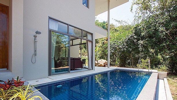 Ett modernt hus med en swimmingpool, stora fönster och en uteplats.