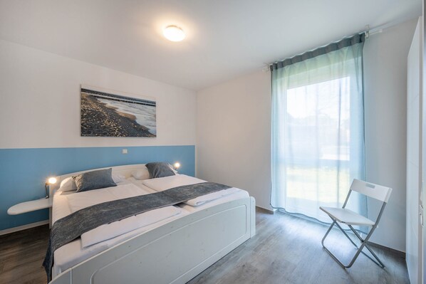 A bedroom with a bed, a chair, a window with curtains, a picture on the wall, and a ceiling light.