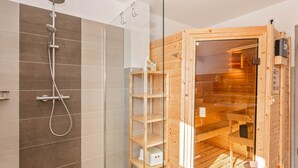A modern bathroom with a shower, a glass-enclosed sauna, and wooden shelves. - Apartment Himmelblau EG (Loddin)