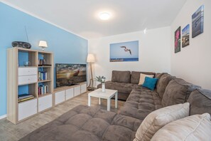 A modern living room with a sectional sofa, a flat-screen TV, a bookshelf, and a painting of a seagull.