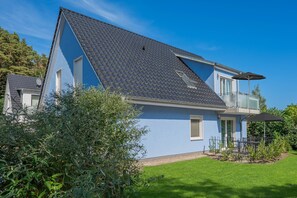 Une maison à deux étages avec un toit en pente, un balcon et un petit jardin.