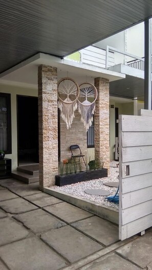 Un espace extérieur moderne agrémenté d’un mur en pierre, d’une décoration en macramé suspendue, d’une chaise noire et d’un pot de fleurs avec des plantes.