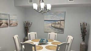 A dining room with a round table, six chairs, a chandelier, and wall art. - Brighton towers.Stay were the view is Beautiful.2 miles to Tanger Outlets!! (Myrtle Beach)