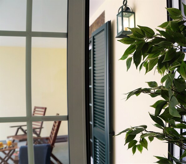A room with a view through a window, a door with shutters, and a hanging lantern.