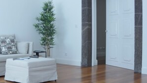 A modern living room with a wooden floor, a white sofa, a small table, and a potted plant. - Apartment B - Heritage Apartments (Funchal)