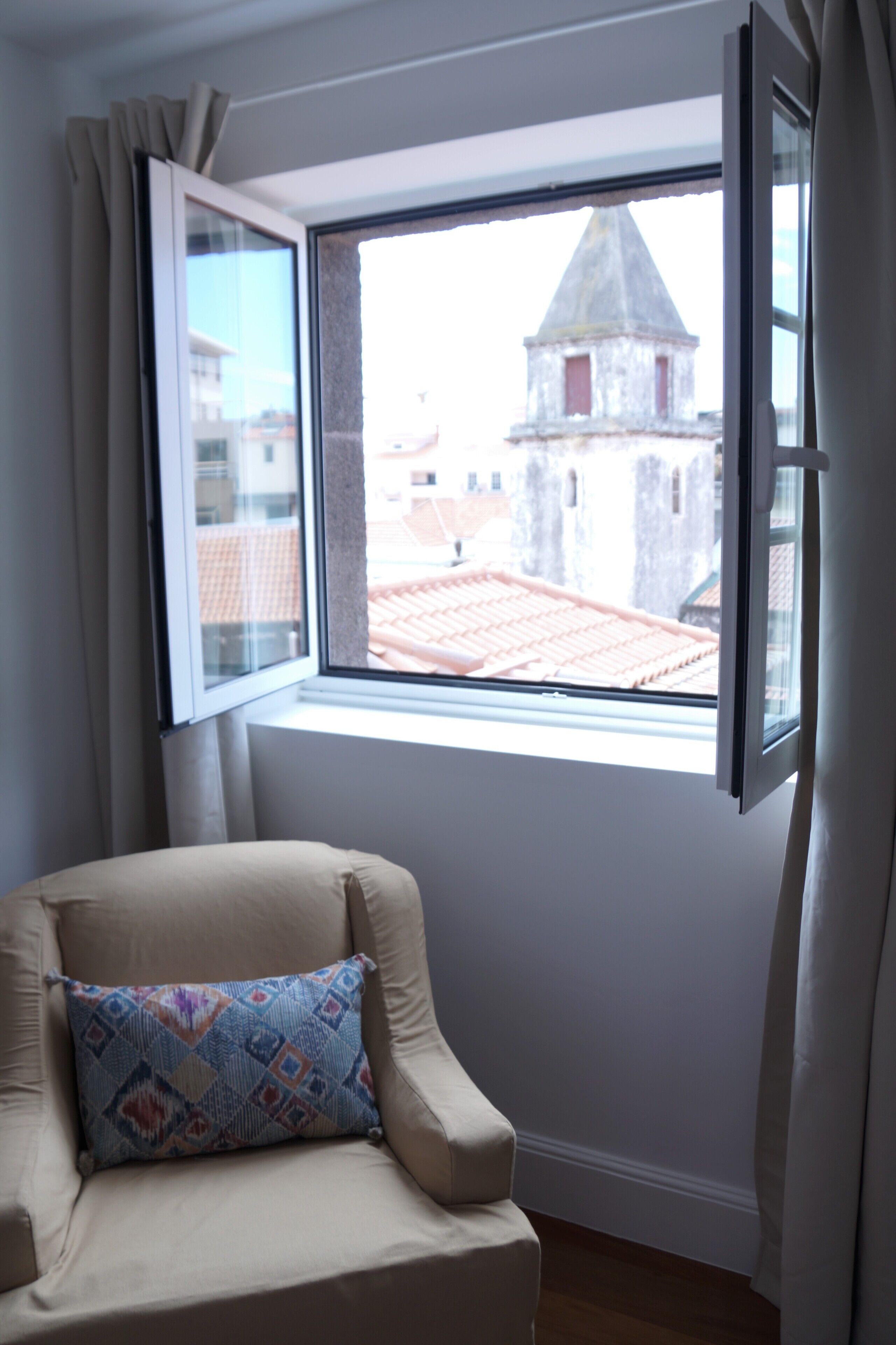 A room with a window overlooking a building with a red-tiled roof.