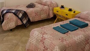 Een slaapkamer met twee bedden, een kroonluchter, een radiator en een klein tafeltje met een geel nachtkastje.