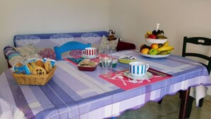 Een eettafel gedekt met diverse etenswaren, waaronder fruit en brood, en een mandje gebak.