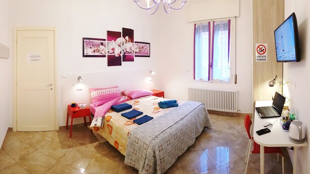 Een slaapkamer met een bed, een bureau, een stoel, een televisie en een raam met gordijnen.