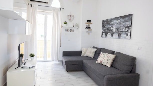 A modern living room with a grey sectional sofa, a white TV stand, and a large black-and-white cityscape painting on the wall. - Nicla's Home - Near Trastevere Station (Roma)
