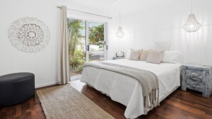A bedroom with a bed, a nightstand, a chair, a ceiling fan, and a view through a glass door. - Beach Cottage Lennox Head (Lennox Head)