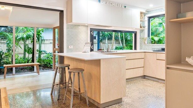 A modern kitchen with a central island, bar stools, and a view of a tropical garden. - Beach Cottage Lennox Head (Lennox Head)