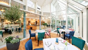 A modern restaurant with glass walls, wooden floors, and blue chairs. - Stadthotel Borken by Hackmann (Borken)