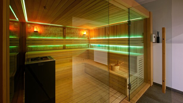 A sauna with wooden walls, glass doors, and green ambient lighting. - Stadthotel Borken by Hackmann (Borken)