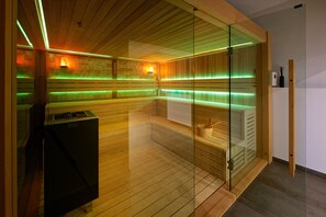 Una sauna con paredes de madera, puertas de vidrio e iluminación ambiental verde.