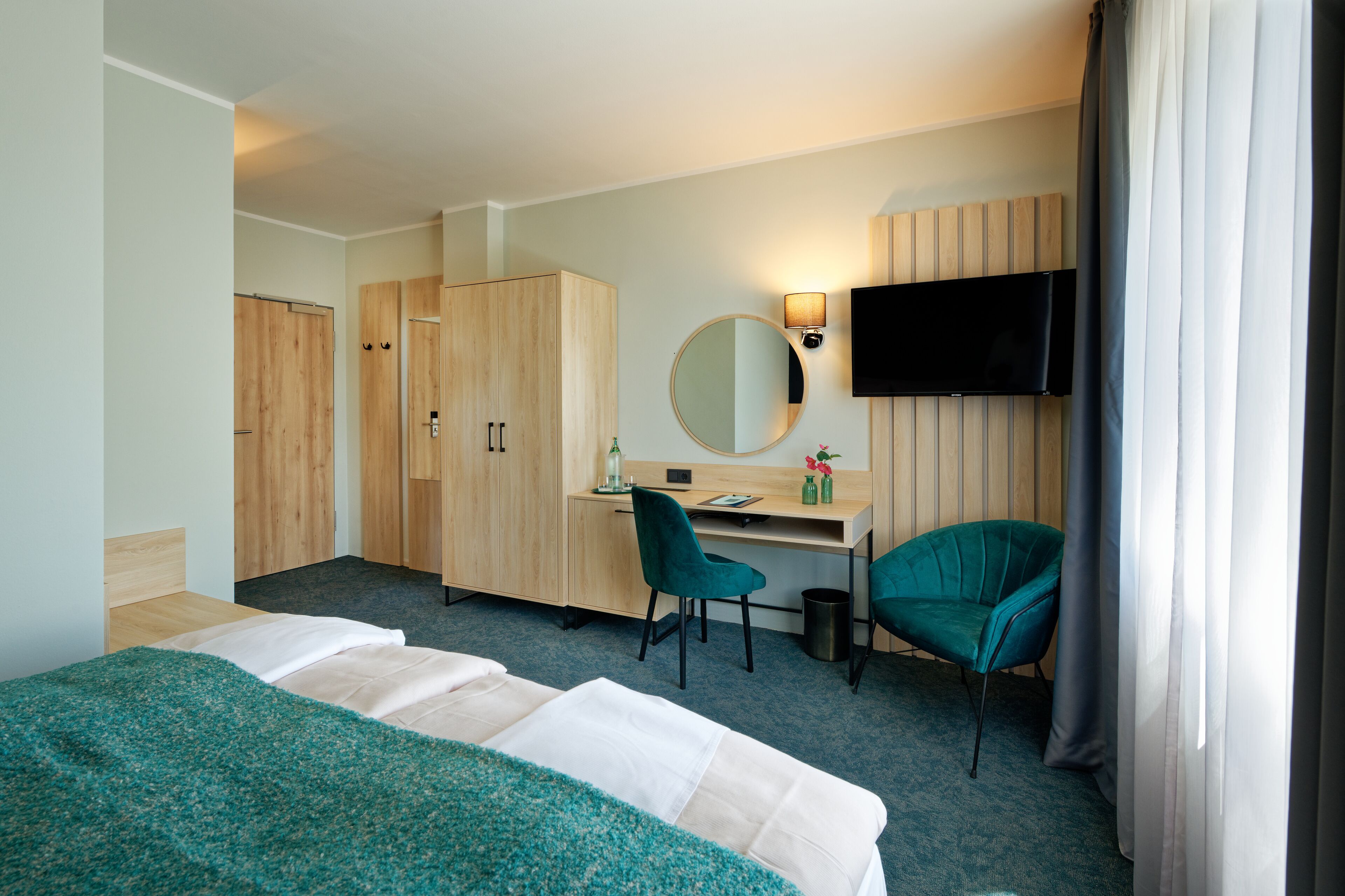 A hotel room with two beds, a desk, a chair, a TV, and a wardrobe.