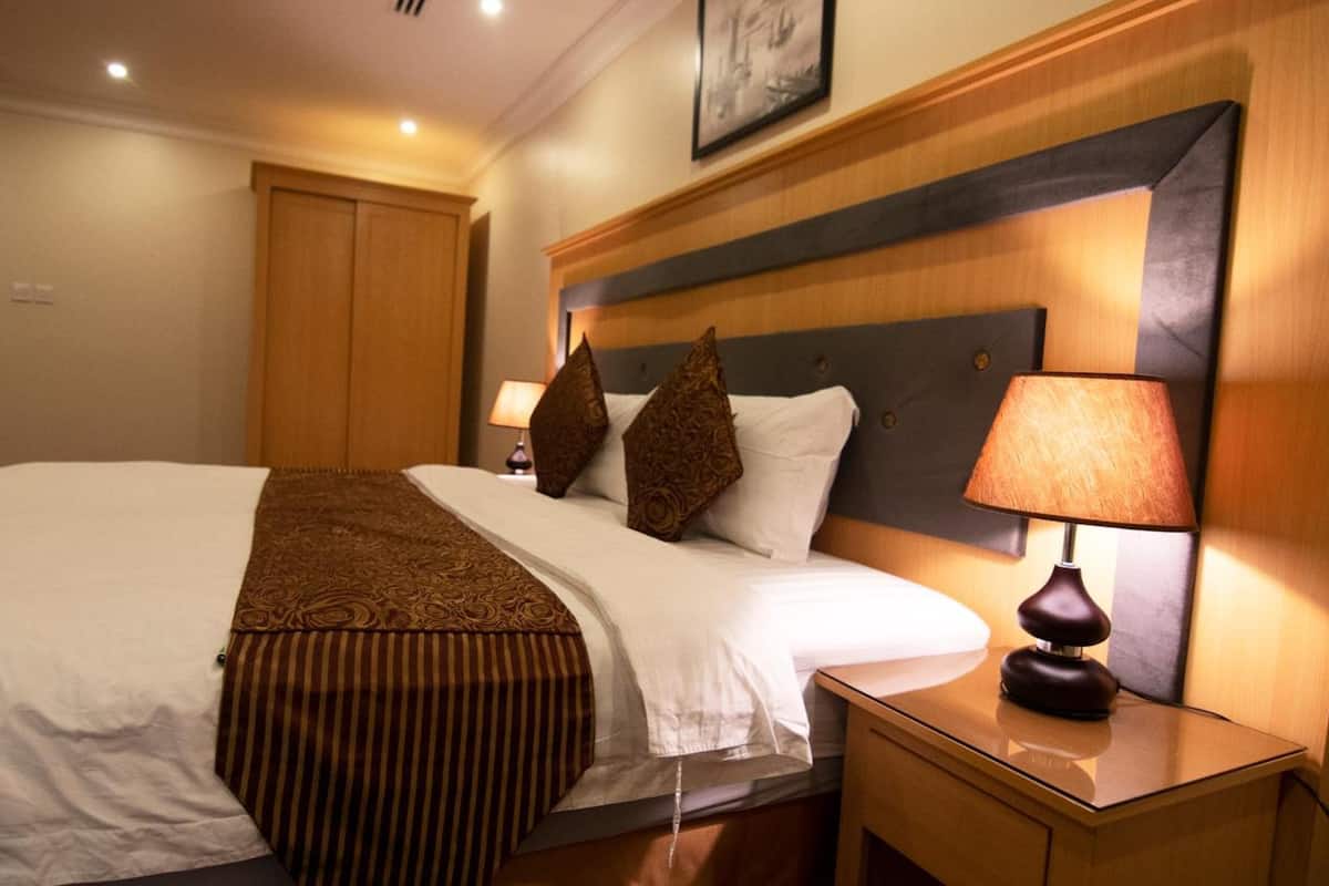 Une chambre d’hôtel avec un grand lit, une tête de lit en bois, une lampe de chevet et une table de chevet.