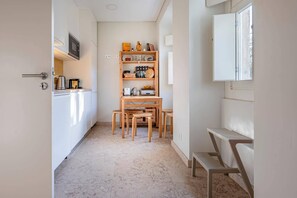 Una cocina estrecha con una mesa y sillas de madera, un estante empotrado con utensilios de cocina, y un ventanal con vistas.