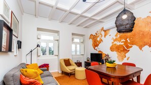 Una sala de estar moderna con un sofá gris, sillas rojas, una mesa de comedor de madera y un mural con un mapa del mundo.