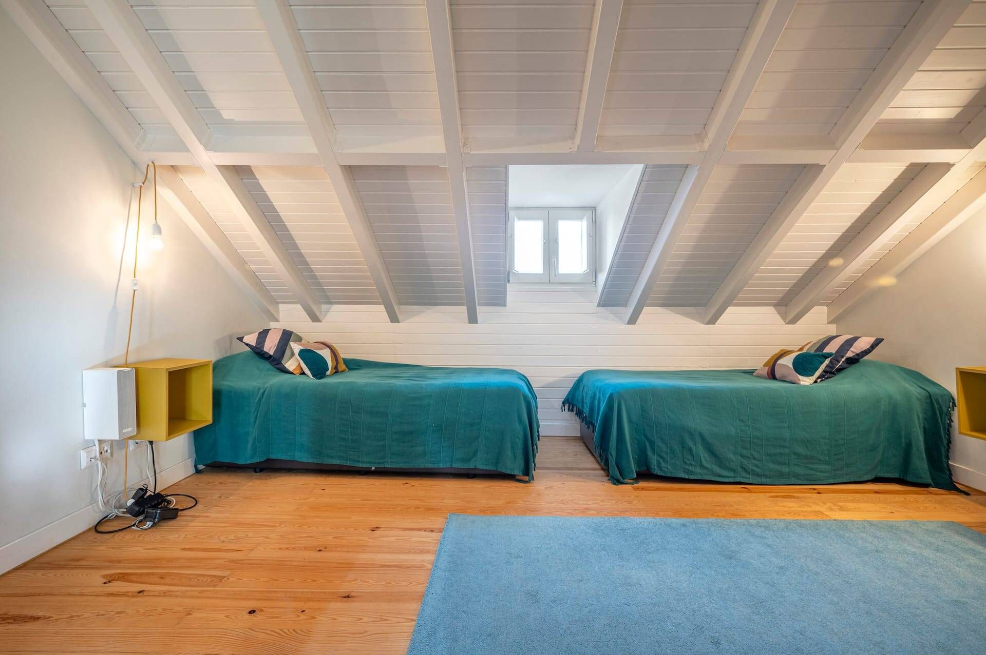 A room with two beds, a skylight, and a wooden floor.