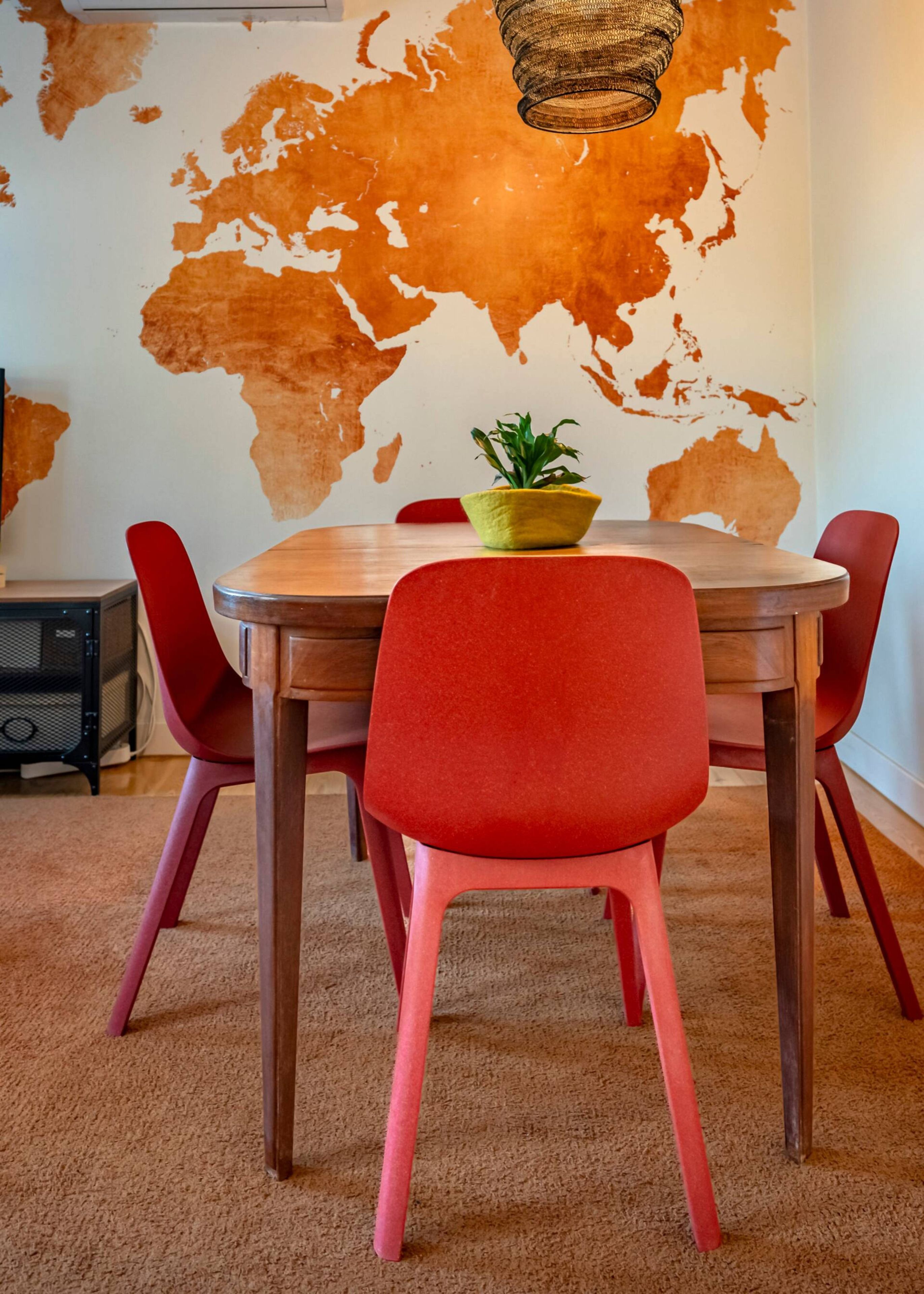 A dining area with a wooden table, red chairs, a yellow plant, and a world map on the wall.