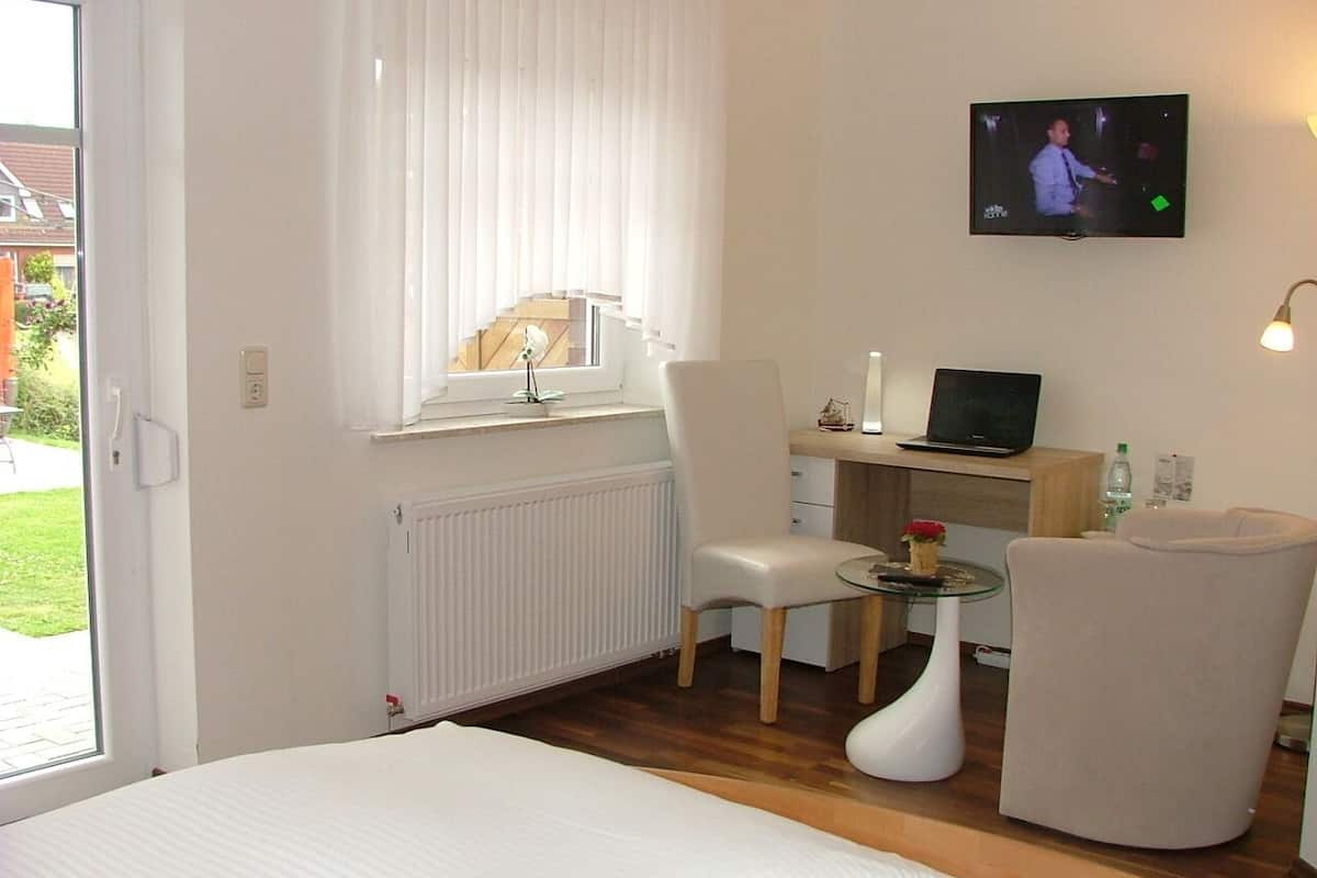 A hotel room with a bed, a desk with a computer, a TV, and a chair.
