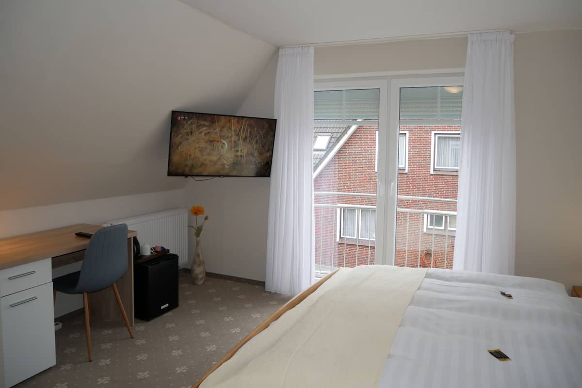 A hotel room with a bed, a desk with a chair, a television, and a window with curtains.