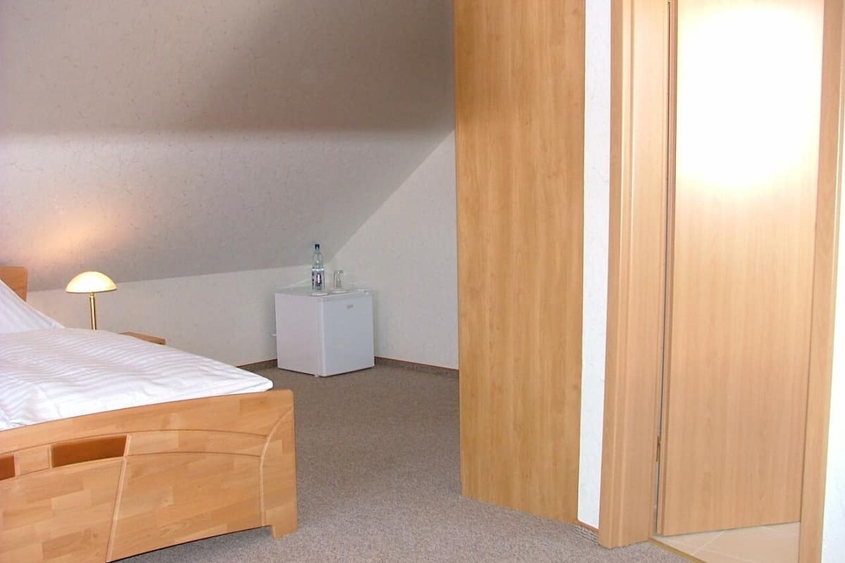 A bedroom with a wooden bed, a bedside table with a lamp, a small white nightstand, and a wooden wardrobe.