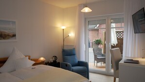 A hotel room with a bed, a desk, a chair, a lamp, and a view of the outside. - Hotel Garni Thule (Wittmund)