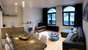 A modern living space with a dining area, sofa, and large windows.