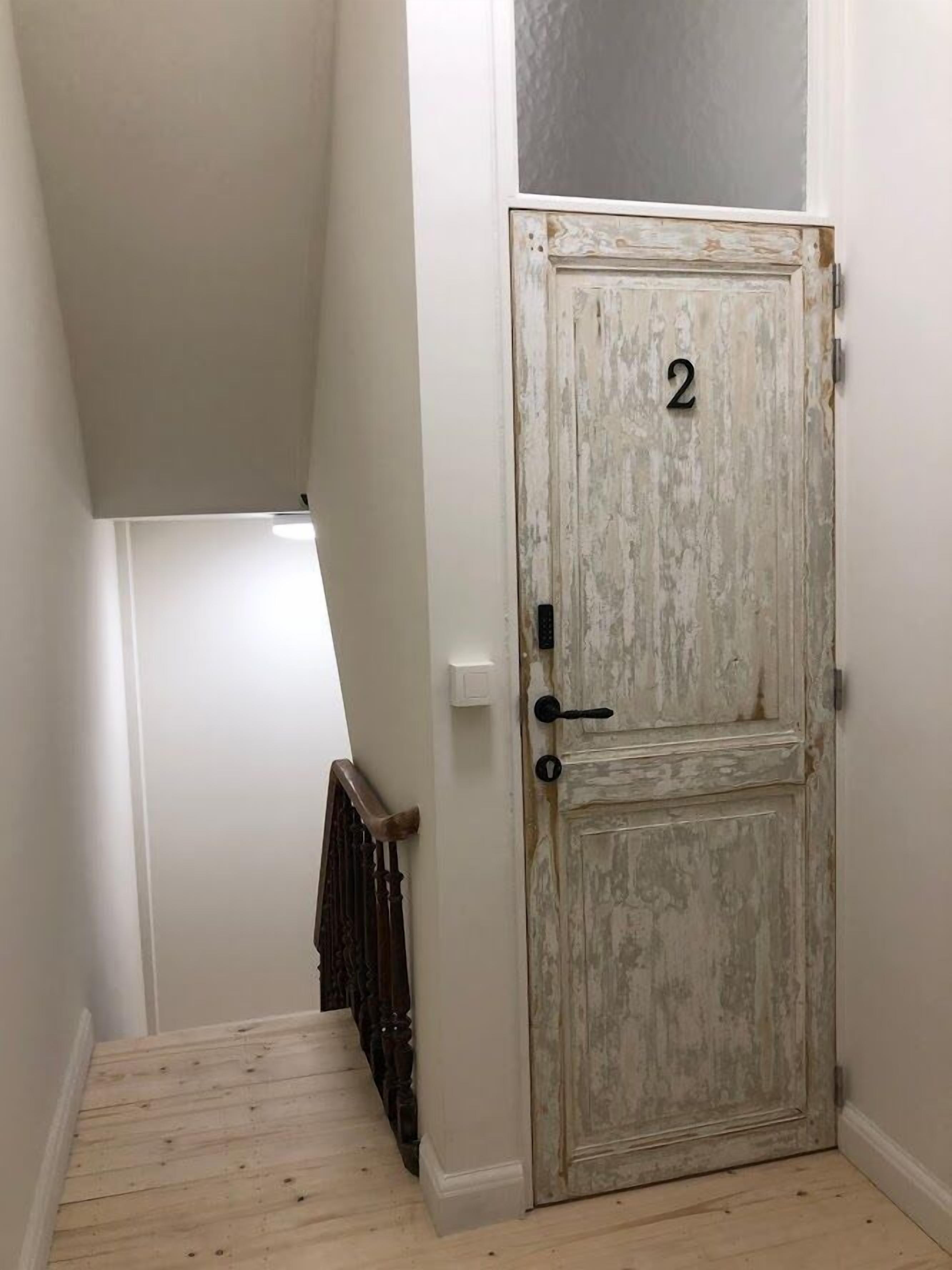 A hallway with a rustic wooden door marked with the number 2, a radiator, and a wooden staircase.