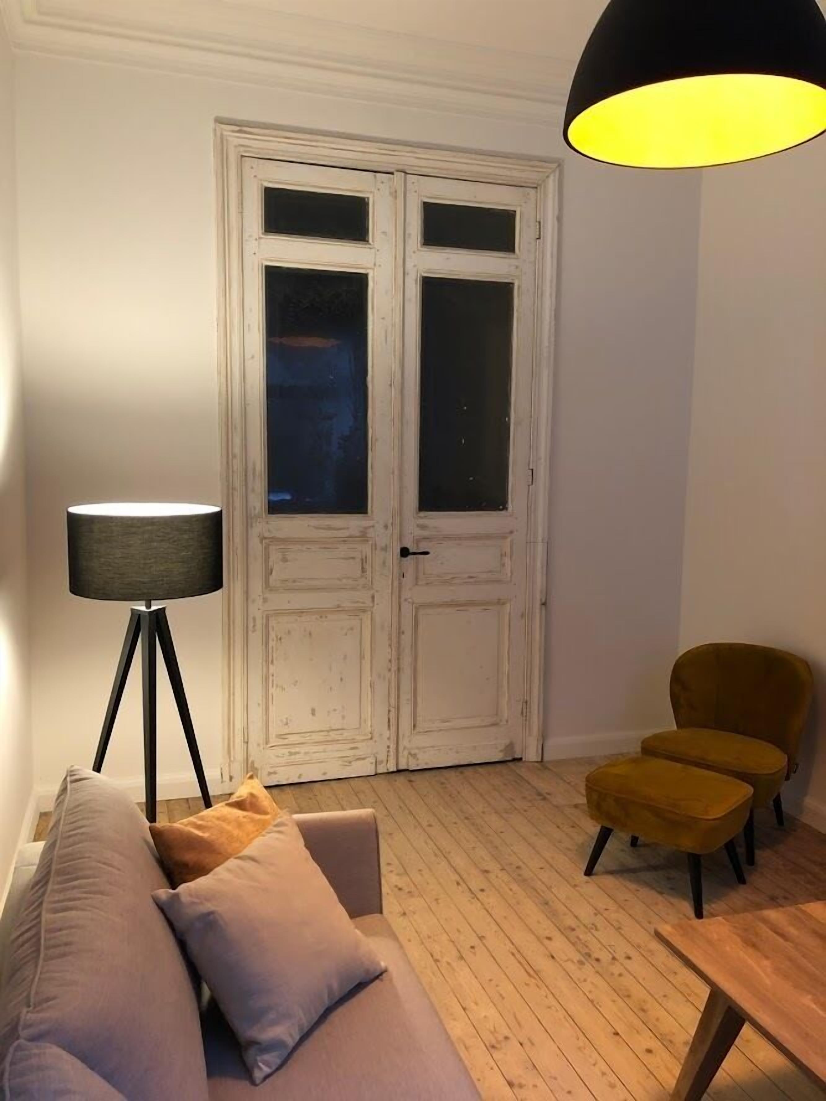 Une pièce avec une porte blanche, un lampadaire, un canapé, une petite table et une chaise.