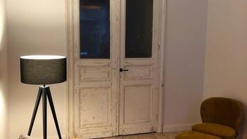 Une pièce avec une porte blanche, un lampadaire, un canapé, une petite table et une chaise.