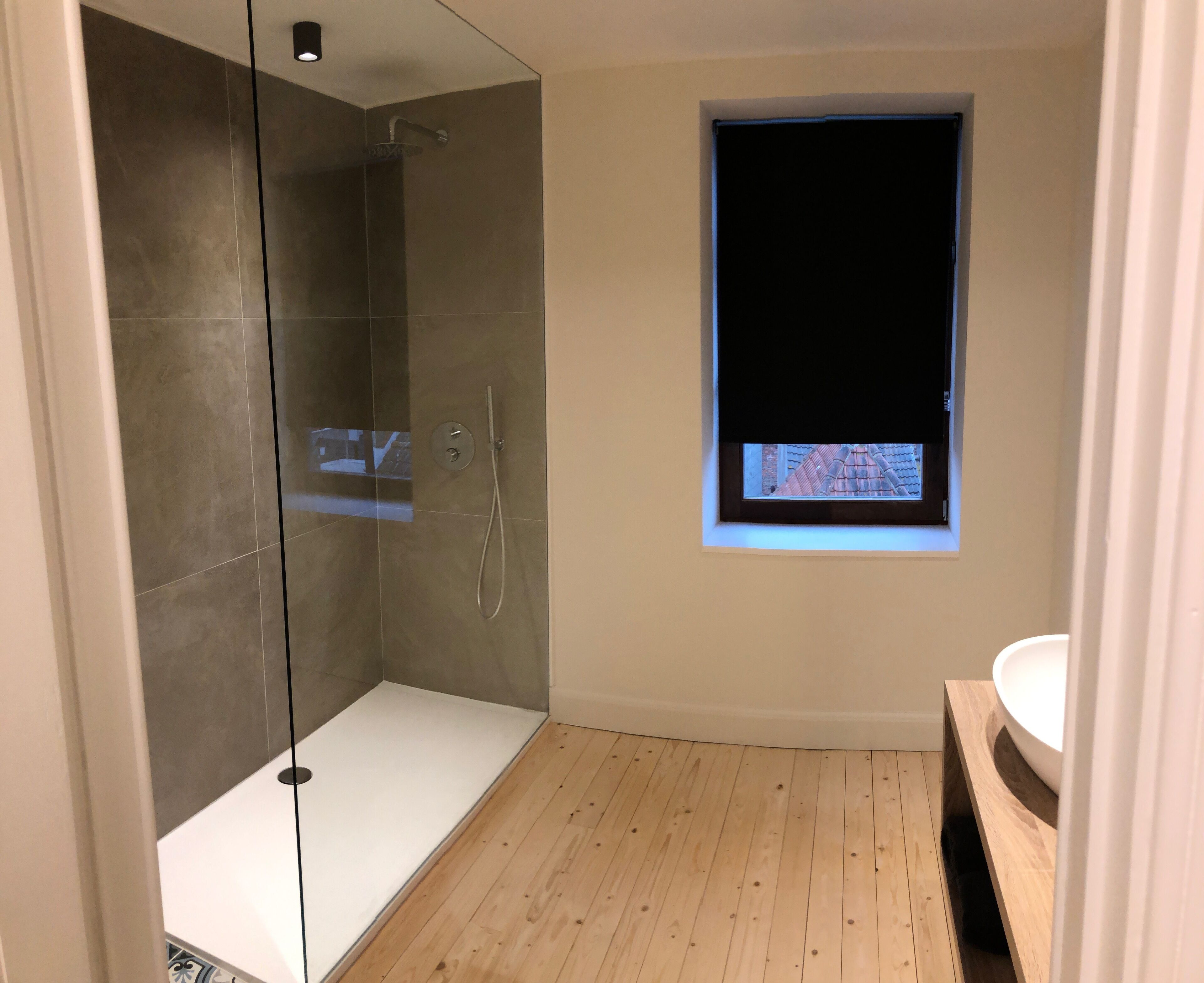 A modern bathroom with a glass-enclosed shower, a small window, and a wooden floor.