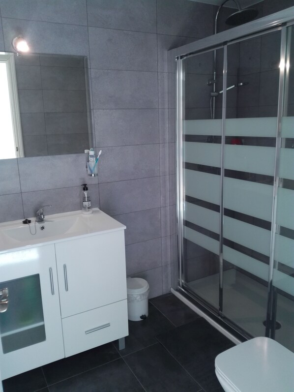 A modern bathroom with a white vanity, a glass shower enclosure, and a mirror above the sink.