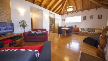 Un vaste espace de vie doté d’un plafond en bois, d’un téléviseur, d’un canapé rouge, d’une table à manger en bois avec des chaises et d’une sculpture en bois.