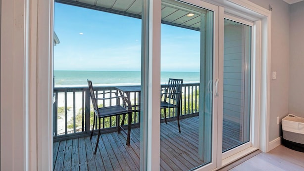 A room with a sliding glass door leading to a balcony with a view of the ocean.