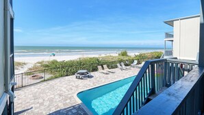A pool area with a view of the beach, outdoor seating, and a clear sky.