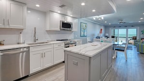 A modern kitchen with white cabinetry, a central island, and a dining area with a view of the ocean.