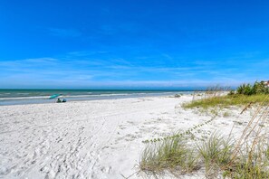 En strand med vit sand, en klarblå himmel och några få personer i fjärran.