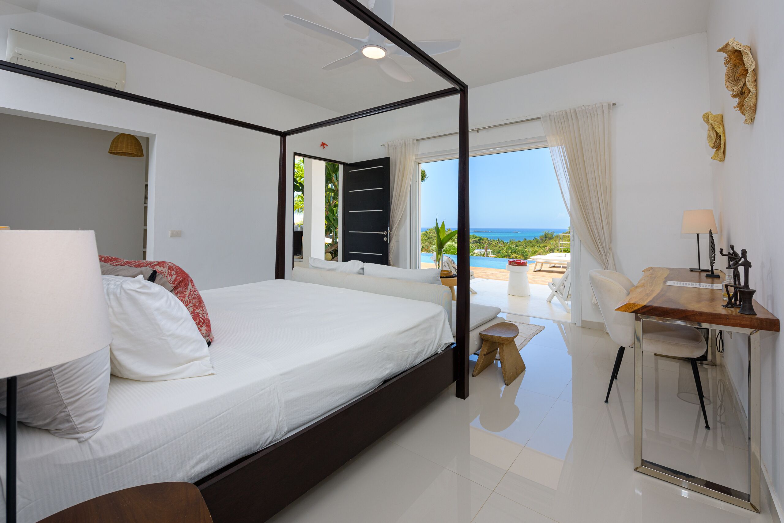 A modern bedroom with a large bed, a desk, and a view of the ocean.