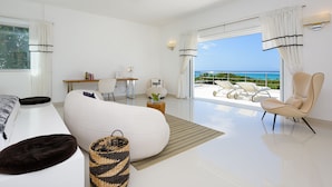 A modern hotel room with a large bed, a seating area with a sofa and armchairs, a small table, and a view of the ocean. - Fabulous Experience AC, Gym, Chef and Staff Available  (Las Terrenas)