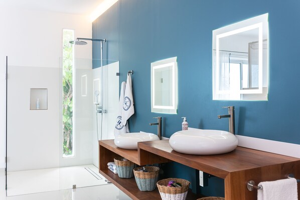 A modern bathroom with two sinks, a glass shower enclosure, and a wooden vanity. - Fabulous Experience AC, Gym, Chef and Staff Available (Las Terrenas)