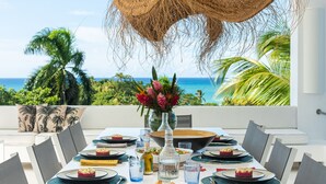 A dining table set for four with a view of the ocean, a hanging basket, and a ceiling fan. - Fabulous Experience AC, Gym, Chef and Staff Available  (Las Terrenas)