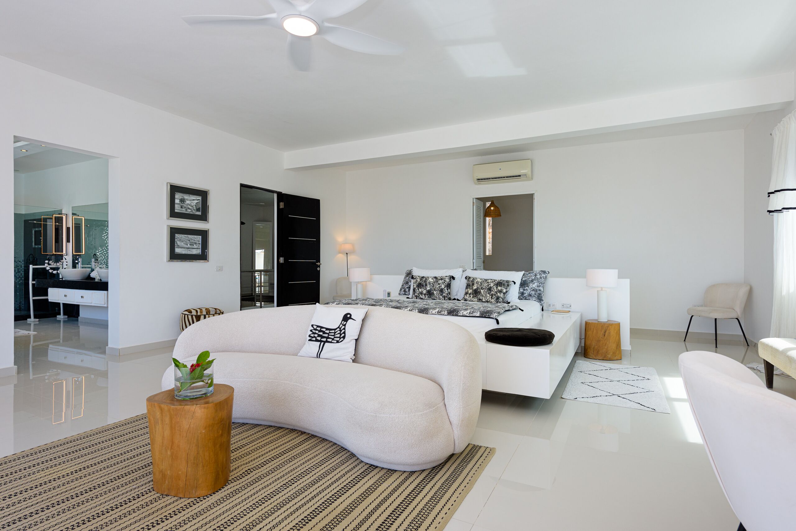 A modern bedroom with a large bed, a wooden side table, and a white armchair.