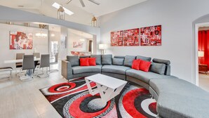 Una sala de estar moderna con un sofá seccional gris, cojines rojos, una mesa de centro blanca y una alfombra estampada en rojo y negro.